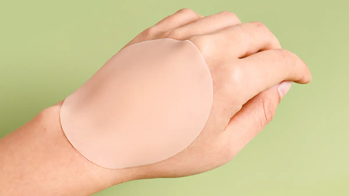 Back of a hand wearing a thin nude silicone nipple cover, showing the feathered edge against skin