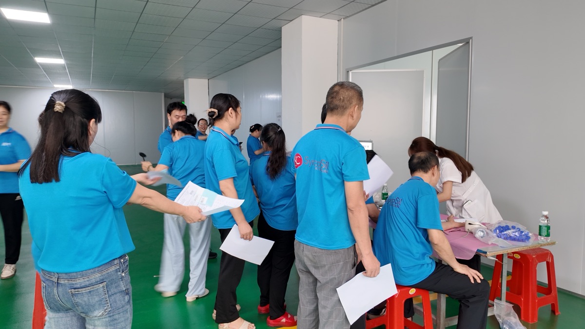 Employees holding examination forms while waiting at a registration table during Xinke 2026 employee health check-up